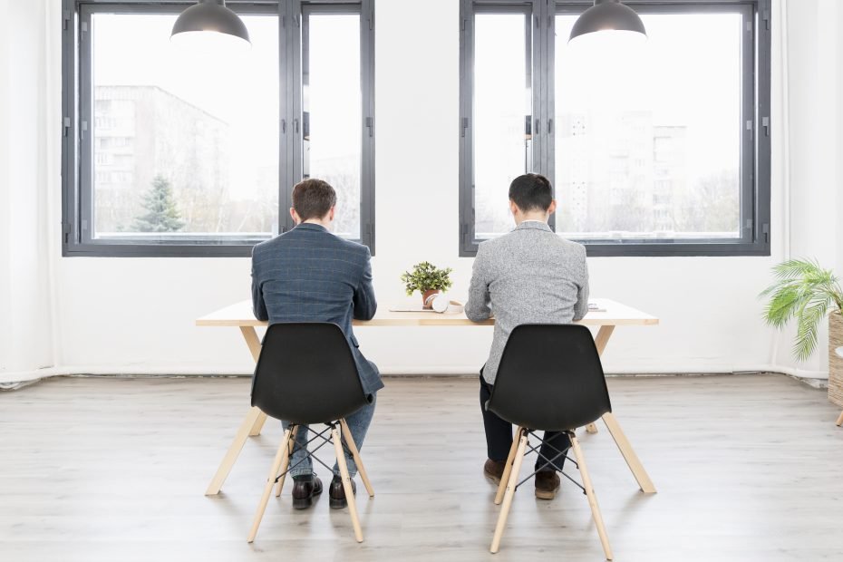 Two professionals sitting at a table in a bright office, engaged in an interview.